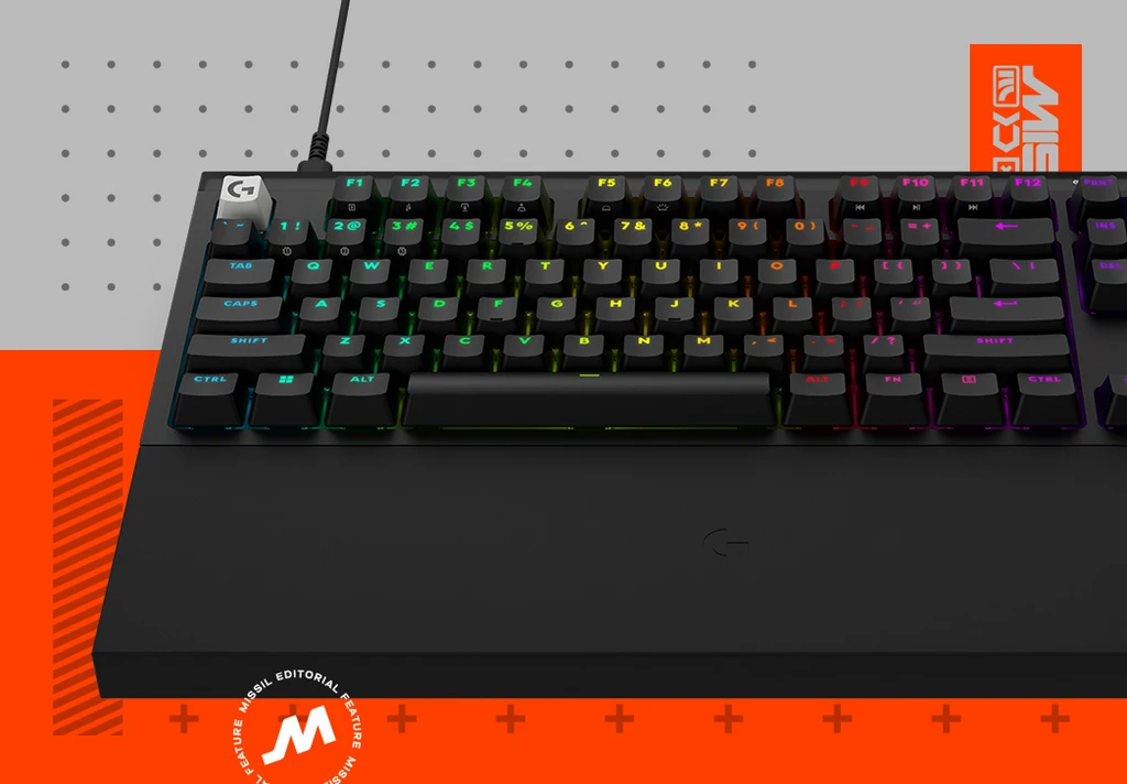 Svart mekaniskt gamingtangentbord från Logitech G med RGB-belysning i regnbågsfärger och stort handledsstöd, mot grå och orange bakgrund med MISSIL-grafik.
