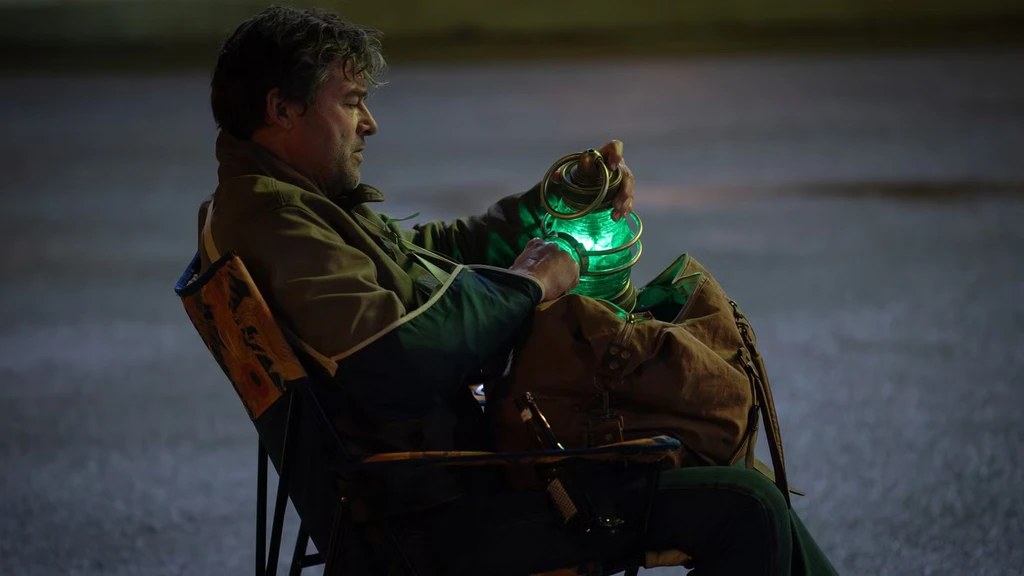 Hal Jordan sitter i en fällstol på en mörk parkering nattetid och håller en glödande grön lykta i famnen, med en packad väska bredvid sig, i serien Lanterns.