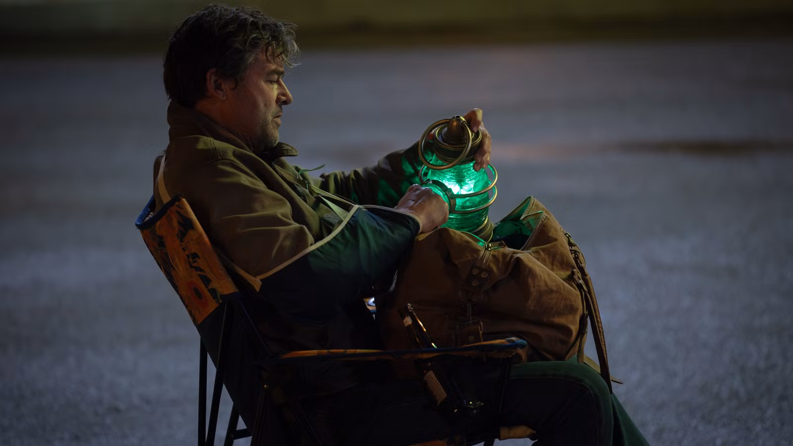 Hal Jordan sitter i en fällstol på en mörk parkering nattetid och håller en glödande grön lykta i famnen, med en packad väska bredvid sig, i serien Lanterns.