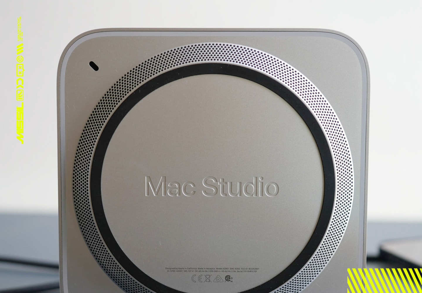 Undersidan av en Mac Studio med instansad text, en rund ventilationsring av små hål och en svart gummiring mot en ljus bakgrund.