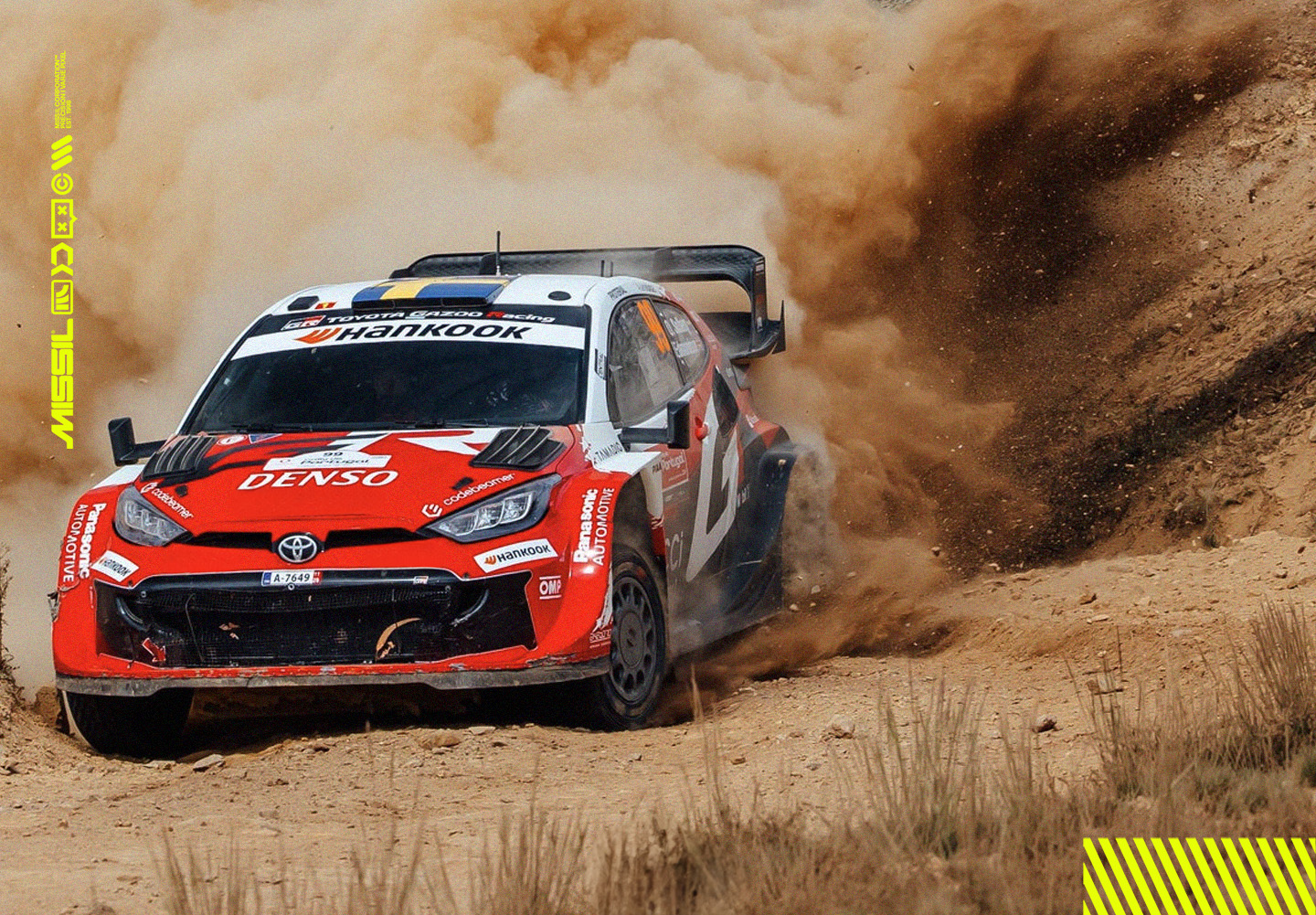 Röd och vit Toyota GR Yaris rallybil slirar genom en gruskurva och virvlar upp ett stort moln av damm.